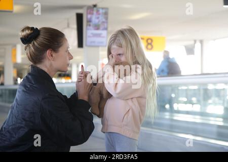 Young woman comforting child lost at the airport who can't find her parents. Mother consoling upset little crying girl which got scared from flight at Stock Photo