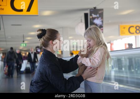 Young woman comforting child lost at the airport who can't find her parents. Mother consoling upset little crying girl which got scared from flight at Stock Photo