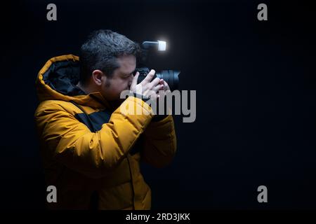 Photographer in a yellow coat taking a photo with flash with a black background Stock Photo