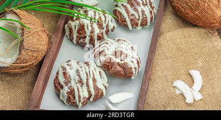 Profiteroles choux pastry buns with coconut cream served in tropical style. Palm leaves, sweet healthy dessert, flat lay, banner format Stock Photo