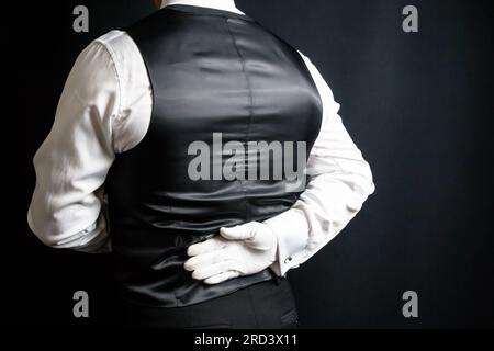Portrait of Back of Butler or Waiter in Vest and White Gloves Standing At Elegant Attention. Service Industry and Professional Courtesy. Stock Photo