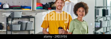 Smiling young multiethnic craftspeople with coffee to go looking at camera while standing and working on project in blurred print studio at background Stock Photo