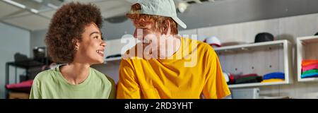 Young and positive multiethnic craftspeople talking and looking at each other while working together in blurred print studio at background, thriving s Stock Photo