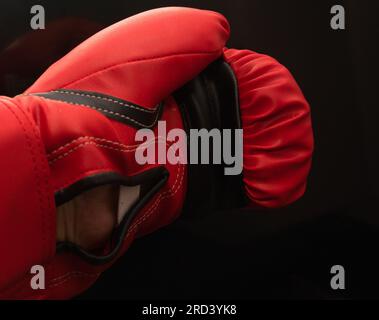 A man's left hand in a red, Lonsdale branded boxing glove; black background, fight, fighting, defend,  aggression, box, combat, hit Stock Photo