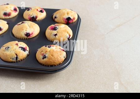 Homemade tasty berries cupcakes with black currant or blueberry in a black metal non-stick cake mold on a beige stone background. Summer baking. Stock Photo