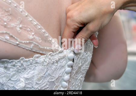 Mother helps her daughter into her wedding dress.  Dress has pearls, lace and cap sleeves.  Image is closeup of mother's hand and brides back. Stock Photo