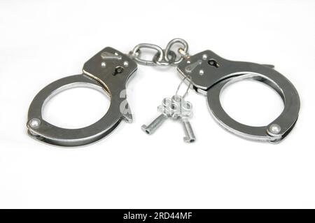 Pair of silver handcuffs lay besides two keys that can unlock them.  Cuffs lay on all white surface. Stock Photo