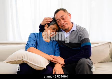 Portrait of healthy senior man and woman embracing and sitting on sofa at home, Happy senior married couple spending time in living room, Grandparents Stock Photo
