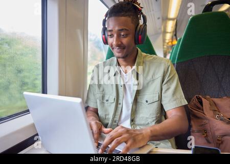 Young Man Commuting To Work Sitting  On Train Working On Laptop Computer Stock Photo
