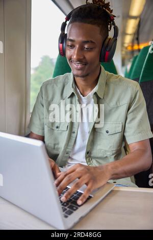Young Man Commuting To Work Sitting  On Train Working On Laptop Computer Stock Photo