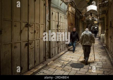 Some men passing through a corridor of the Three Markets, closed due to strike, in the Muslim Quarter of the Old City of Jerusalem Stock Photo