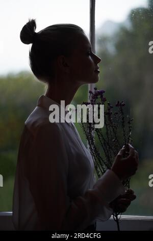 Dawn beauty. A silhouette of a beautiful young woman holding some flowers and enjoying their scent. Stock Photo