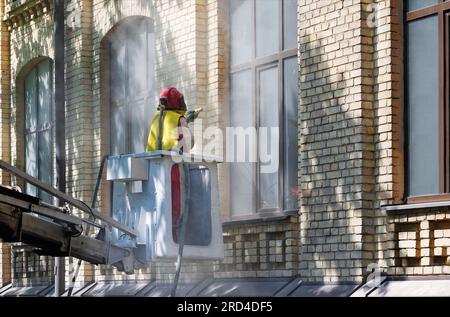 A worker in a protective suit cleans the facade of an old brick house with an industrial sandblaster. Stock Photo
