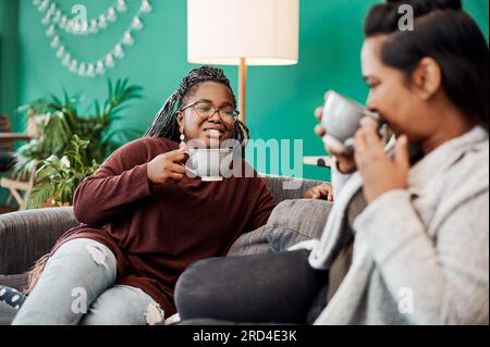 With good coffee comes good conversation. Shot of two young women having coffee and chatting on the sofa at home. Stock Photo