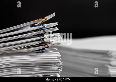Stacks of papers with multicolored paper clips on a dark background Stock Photo