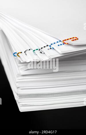 Stacks of papers with multicolored paper clips on a dark background Stock Photo
