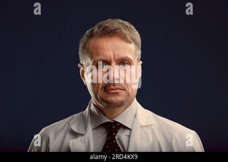 Middle-aged scientist reflects on political barriers and bureaucracy, doubting the system's money-oriented interests. Wears a white shirt, dark patter Stock Photo