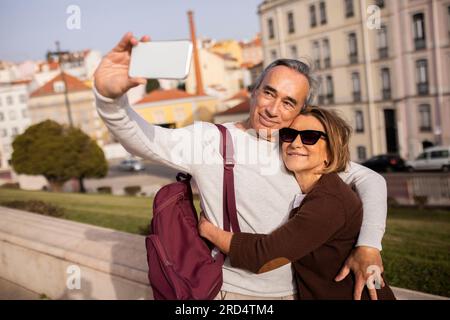 Happy Pensioners Couple With Backpack Making Selfie Using Smartphone Outdoor Stock Photo