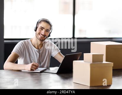Happy Manager Guy With Headset Taking Notes At Laptop Indoor Stock Photo