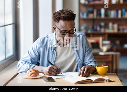 Focused guy student taking notes at table in coffee shop Stock Photo