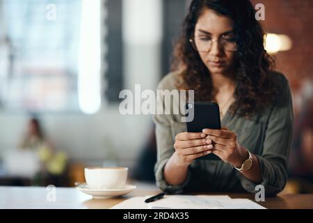 Its a freelancers world and were all living in it. Shot of a young woman using a smartphone while working in a cafe. Stock Photo