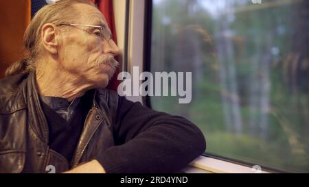 Closeup of elderly man with glasses travels in a train and looks at out the window Stock Photo