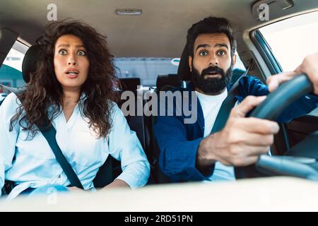 Scared arab couple looking at road with shocked expression, having risk of traffic accident driving car and braking hard Stock Photo