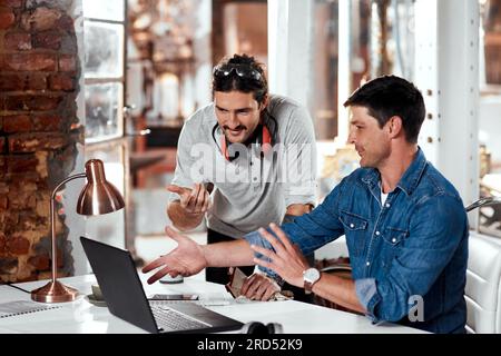 Thats what weve been considering all along. Cropped shot of two young businessmen working together on a laptop in an office inside their workshop. Stock Photo