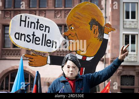 An activist wearing a mask of German Foreign Minister Annalena Baerbock sits on a replica of a tank in front of a speech bubble of German Chancellor Stock Photo