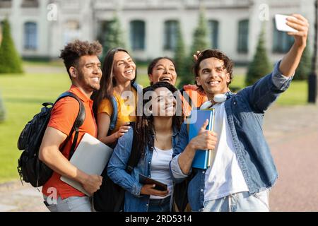 Portrait of happy multiethnic students talking selfie on smartphone outdoors Stock Photo