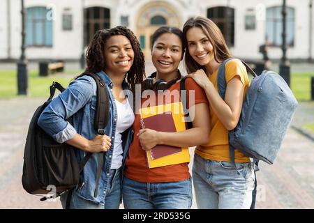 College Friendship Concept. Three Multiethnic Female Students Posing Outdoors At Campus Stock Photo