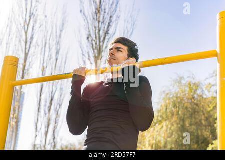 Attractive man doing pull-ups exercises on a crossbar in a public park Stock Photo