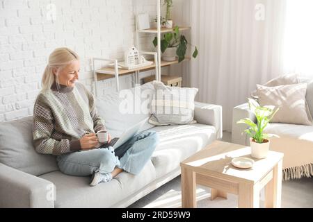 Mature female programmer with cup of coffee and laptop working at home Stock Photo