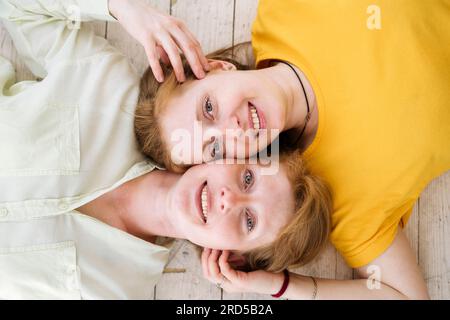 Two red-haired sisters lie cheek to cheek and smile. Similar women with fair skin and freckles.  Stock Photo