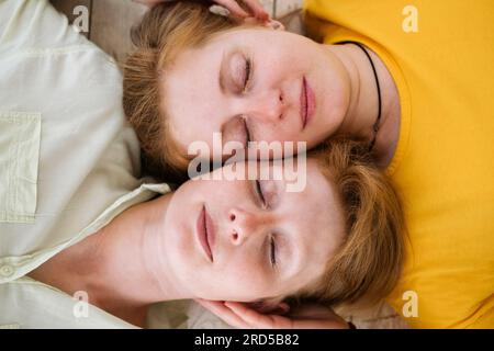 Two red-haired sisters lie cheek to cheek with their eyes closed. Similar women  Stock Photo