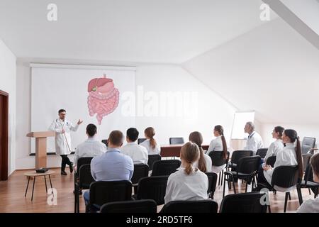 Lecture in gastroenterology. Professors and doctors in conference room. Projection screen with illustration of digestive tract Stock Photo