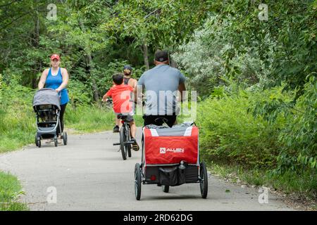 Three Caucasian people riding bikes & one woman walking while pushing a baby carriage. Wichita, Kansas, USA. Stock Photo