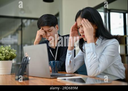 Two serious and stressed Asian office workers are focusing on their co-project together, planning and finding solutions to their project problems. Stock Photo