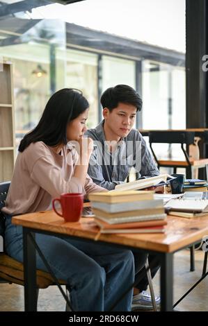 Two serious and focused Asian college students are studying, researching information in a book, and reading books while sitting in a campus library to Stock Photo