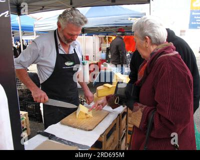 Tasmanian market stall holder and cheese maker slicing a cheddar style cheese for a customer Stock Photo