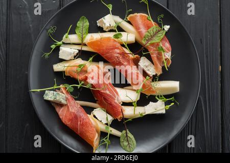 Appetizer of prosciutto, pear and blue cheese on a black plate for the holiday, close-up, top view Stock Photo