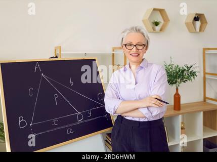 Portrait of happy smiling maths teacher standing by chalkboard in school classroom Stock Photo