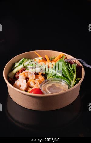 Bowl with shrimps, carrots, cucumbers, beans and vegetables with herbs, on a black background. Healthy food concept Stock Photo