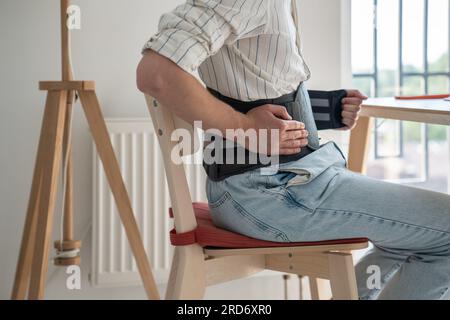 Man sitting at table wearing medical corset for lumbar spine Stock Photo