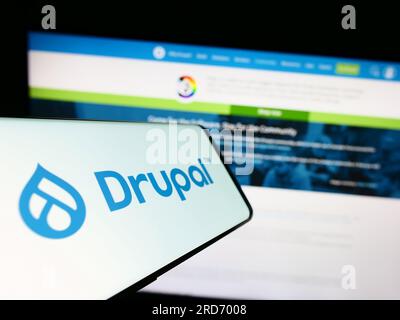 Mobile phone with logo of content management system Drupal on screen in front of website. Focus on center of phone display. Stock Photo