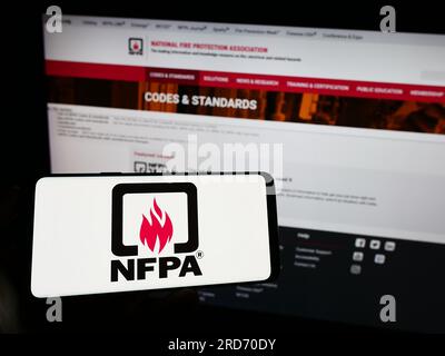 Person holding cellphone with logo of National Fire Protection Association (NFPA) on screen in front of webpage. Focus on phone display. Stock Photo