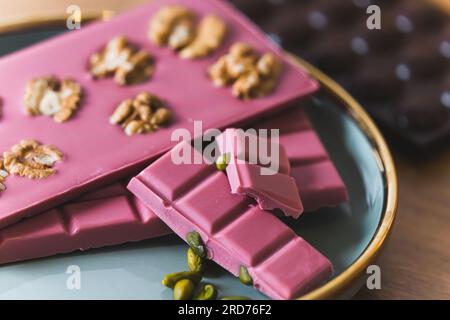 Closeup shot of bars of sweet ruby chocolate with walnuts and pistachios presented on light blue plate. Suggested serving concept. Focus on the foreground with dark chocolate in the background. High quality photo Stock Photo