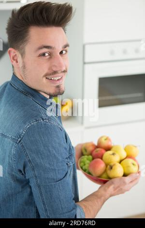 man holding a bowl of apples in the kitchen Stock Photo