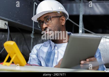 electrician working in roofspace using multimeter and tablet Stock Photo