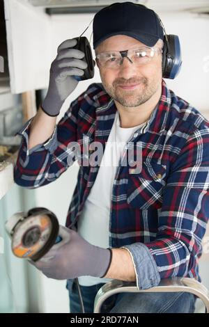 man holding angle grinder lifting an earmuff from his ear Stock Photo